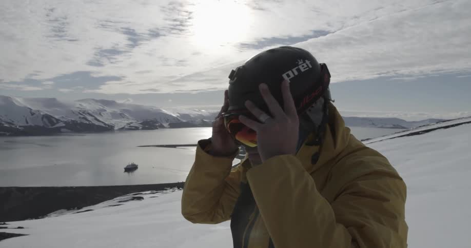 A man in the snow puts his helmet and goggles on in a sunny winter landscape