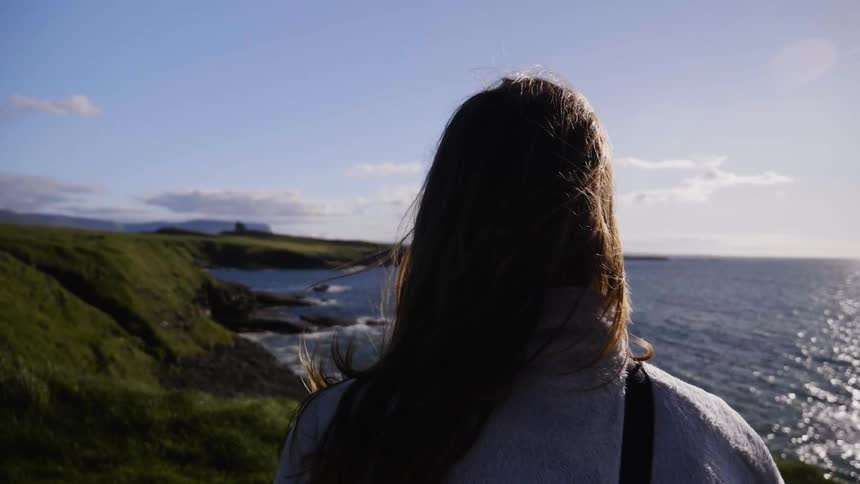 Woman standing on the edge of a cliff looking out at water