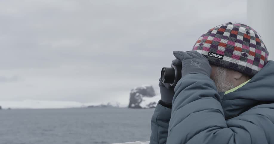 Man with hat looks through camera out at cold water