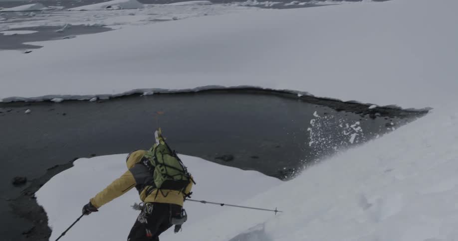 A skier skis down a steep slope towards the water (slow motion)