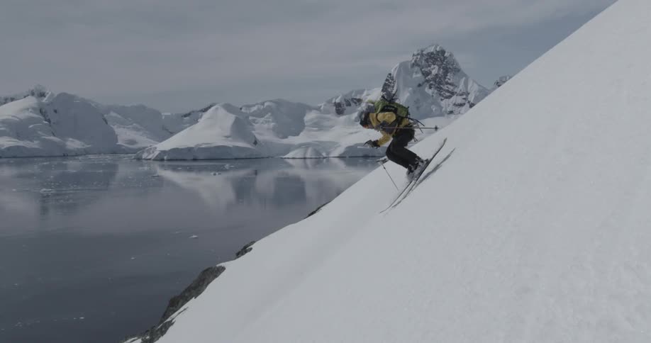 A person skiing downhill near the water in yellow jacket (slow motion)