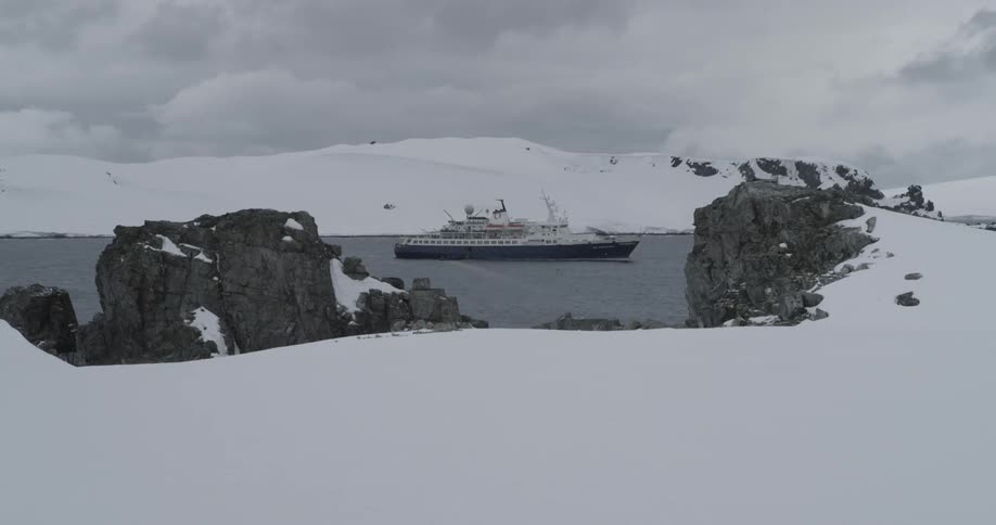A ship sits in the middle of a glaciated ocean inlet surrounded by snow
