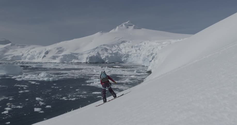 Woman snowboards down a steep sunny slope with floating icebergs in the background