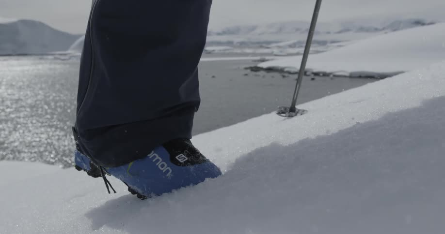 A person's feet walking in the snow with poles near a waterway