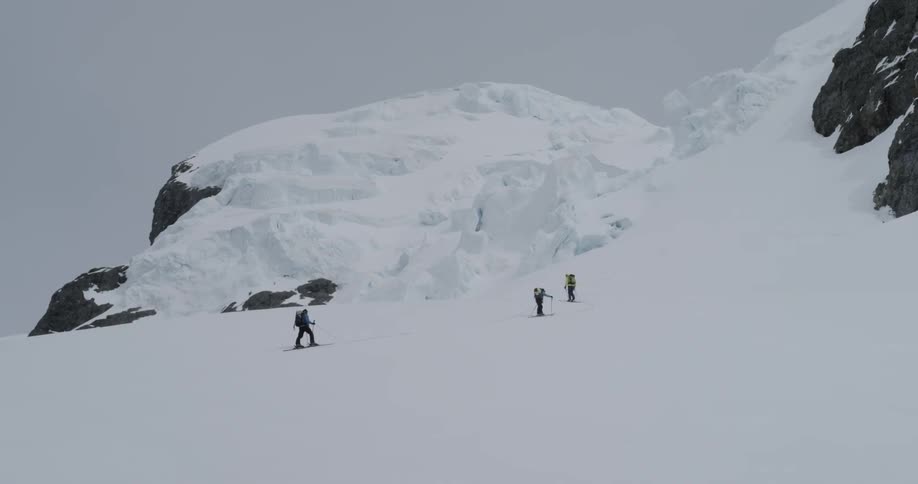Three people hike slowly up a snowy glaciated mountain