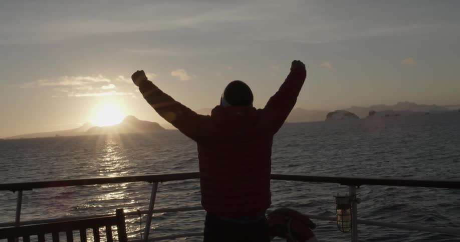 Man looking out over ocean raising his arms at sunset