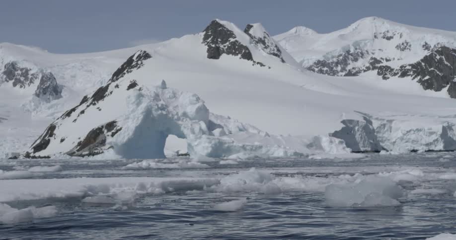 An iceberg forming an arch floats in the cold, harsh water