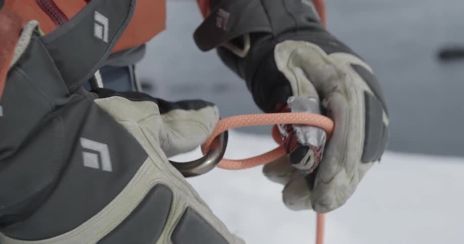 A climber in winter gear is attaching a rope to a carabiner
