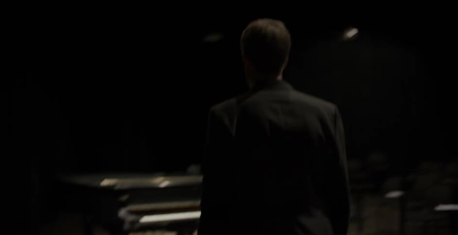 A man walks down a dark hall onto a stage