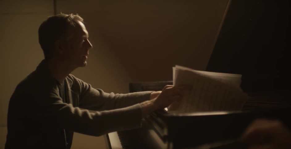A man looks at sheets of music while sitting at a piano