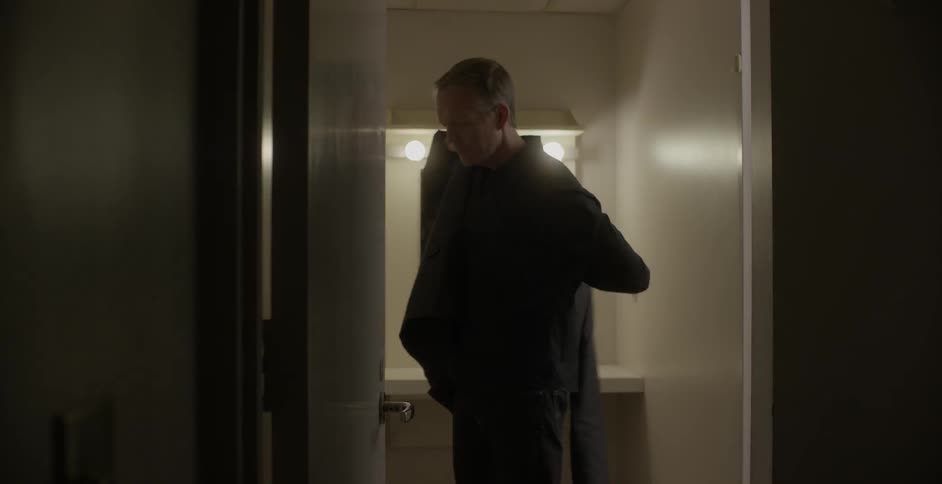 A man walks into a doorway and puts his jacket on