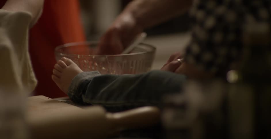 A barefoot toddler sits on the counter while its parent cooks