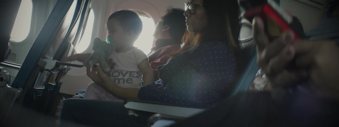 A woman is holding a playing baby as she sits on an airplane