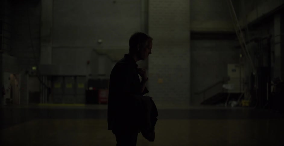 A man stands in a dark room with a jacket in hand