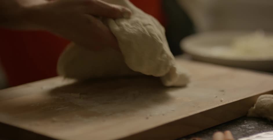 A woman kneads dough on a wood cutting board