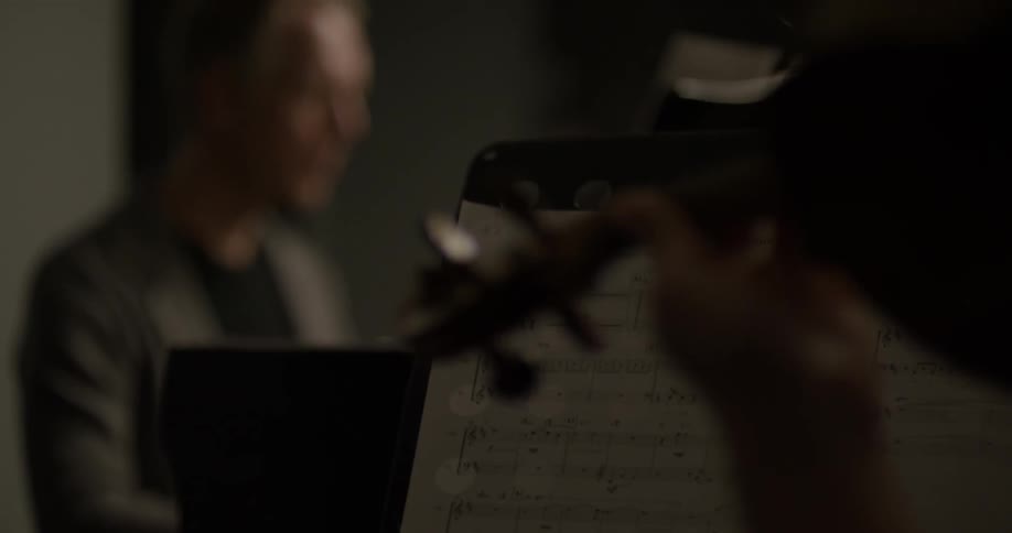 A person holds a violin while a man sits at a piano