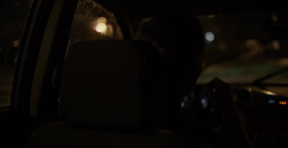 A man is driving at night as it rains