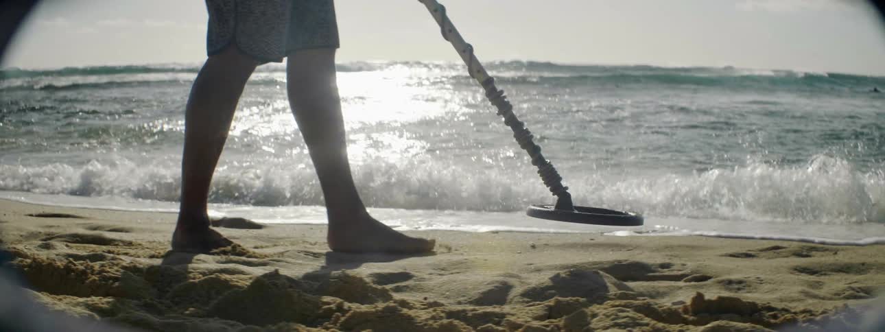A man walks the beach scanning the sand with a metal detector