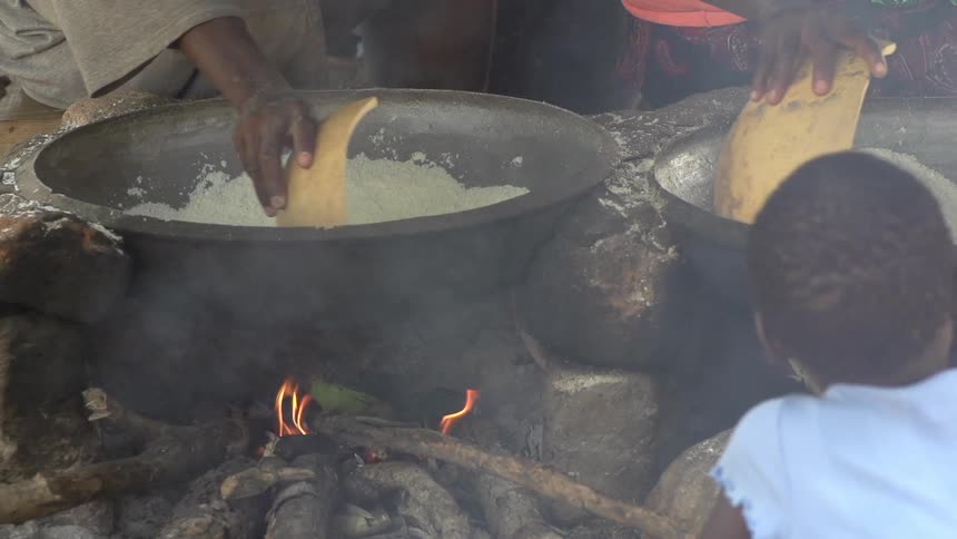White mixture being stirred in large pots over an open fire