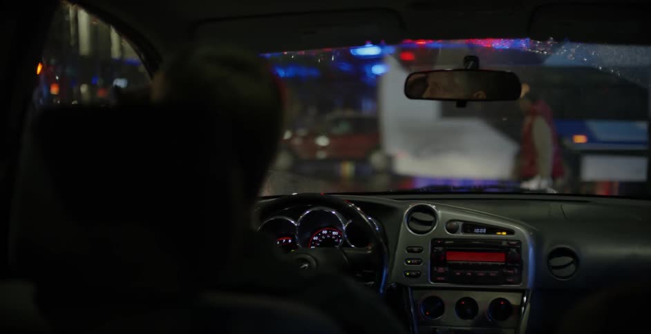 A man drinks coffee in his car while it rains
