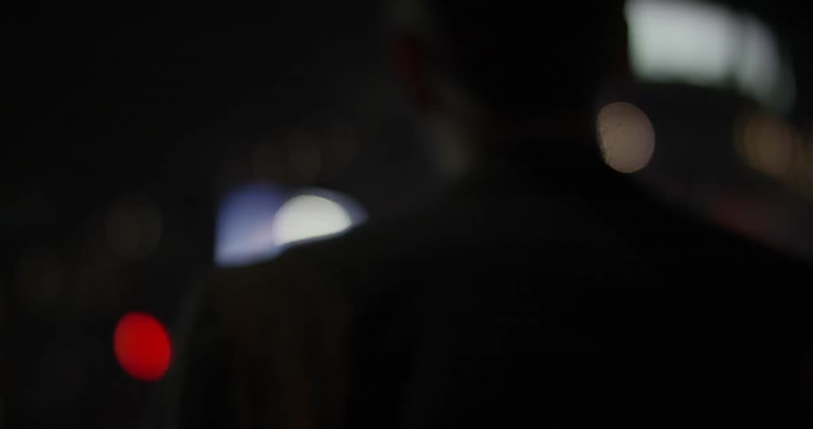 Man standing still in a dark room watching a tv