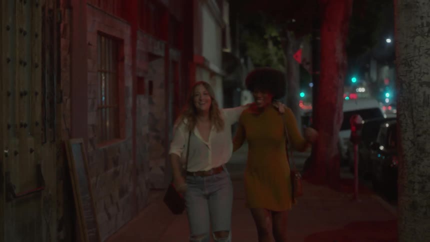Two women hold hands and hug as they run out of a club onto the sidewalk