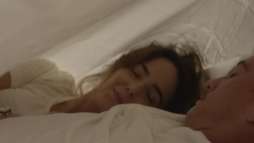 A man and woman cuddle together under the sheets