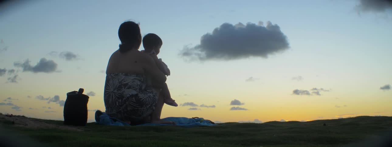 A woman sits down with her child on the beach at dawn