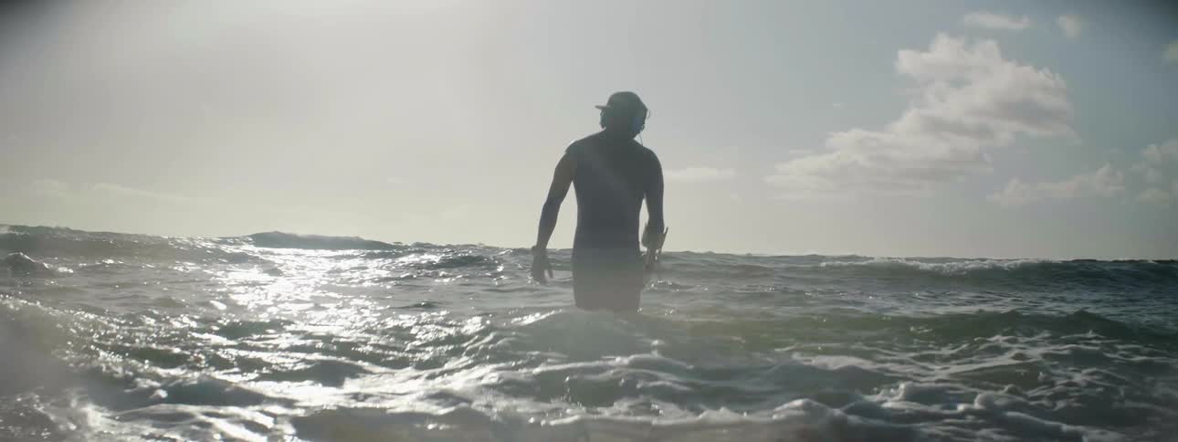 A man using a metal detector wades into the surf searching for treasure