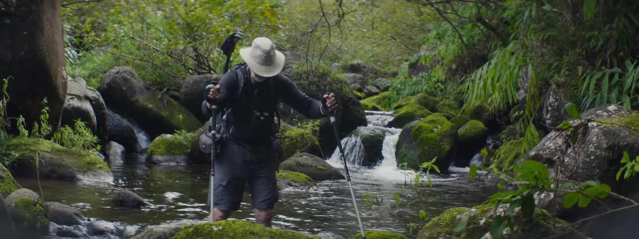 Man walking through a stream using walking sticks