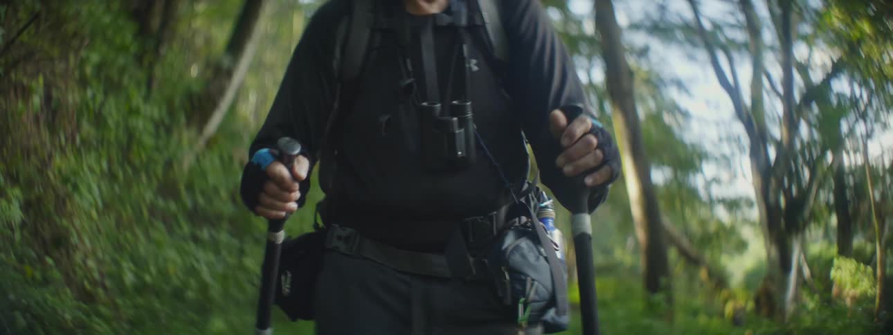 A man uses hiking poles to hike along a path with lots of green foliage