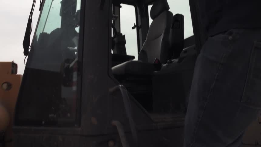 A man jumps up into his tractor