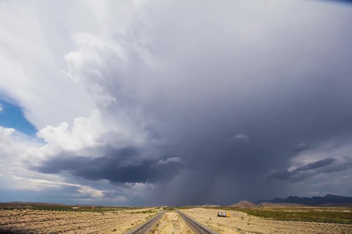 Vehicles drive on a country road with clouds overhead