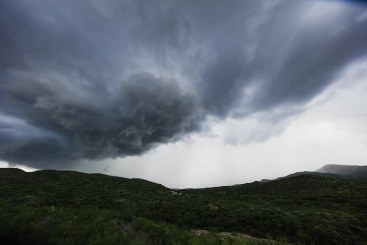 Storm clouds move across and drop rain over hills
