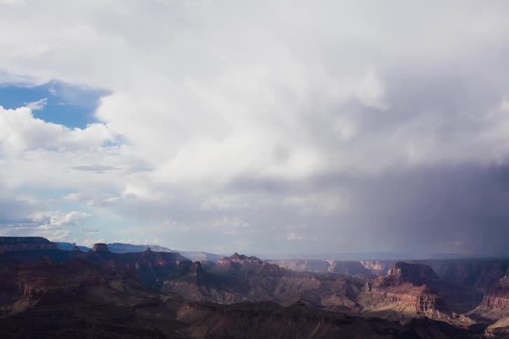Storm clouds move across and drop rain over a canyon