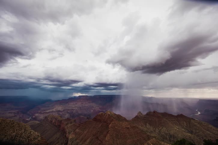 Storm clouds move across and drop rain over a canyon