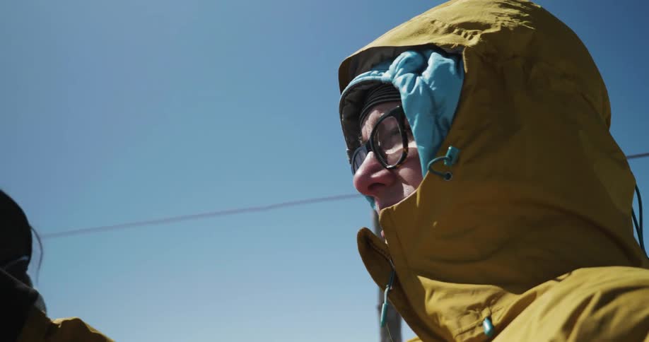 Two people wearing winter gear stand outside on a sunny day