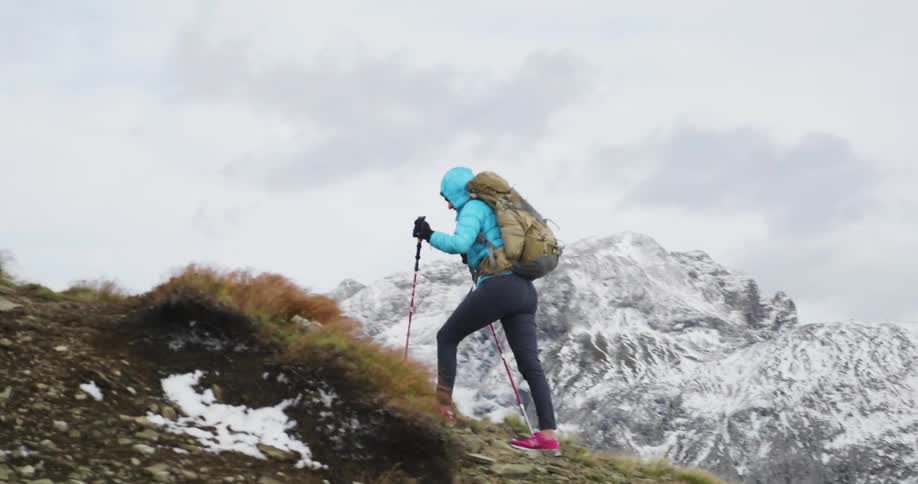A woman in pink shoes hikes a hill with walking poles
