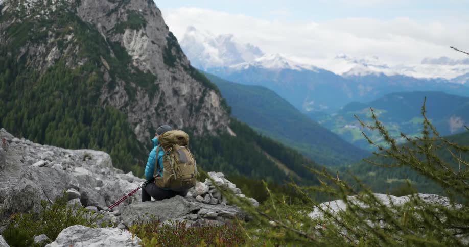 Person wearing a backpack sits on a rock and looks at mountains
