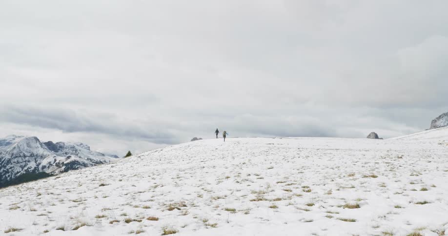 Two women are hiking on a snow-covered hill on a cloudy day