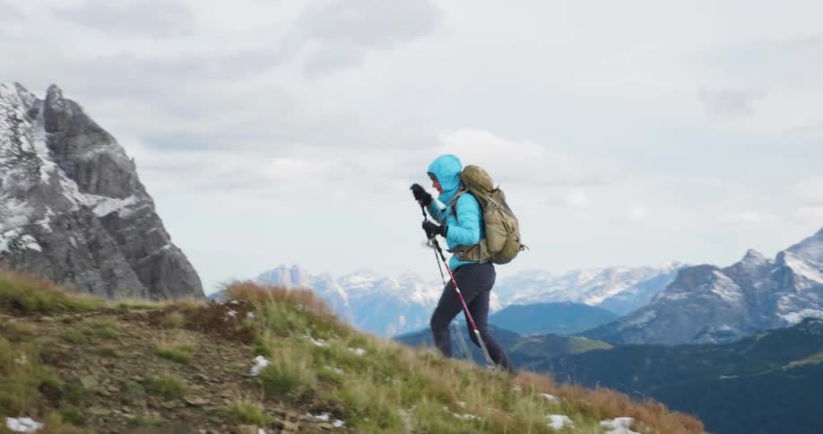 A hiker climbs up a hill on a windy day and stops to look at the mountains