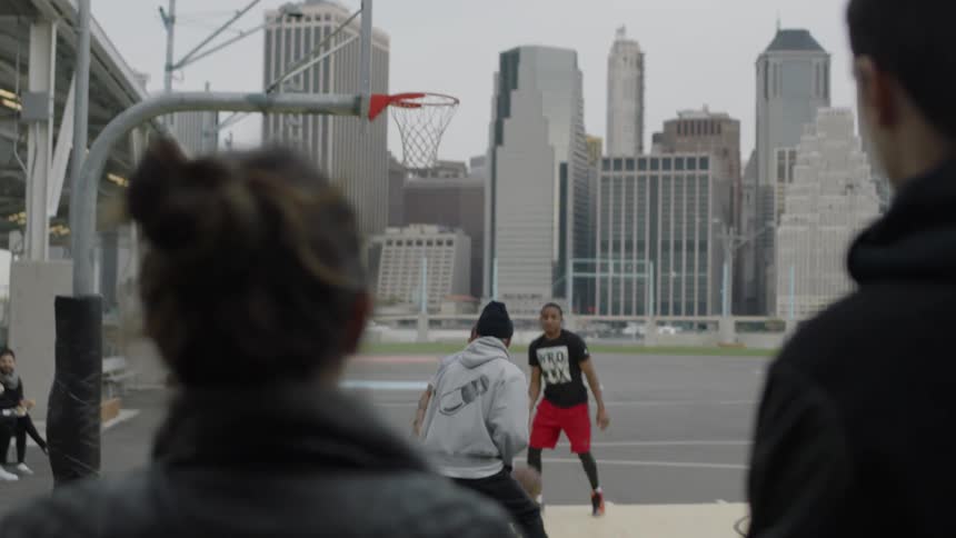 Spectators watch as a group of men play basketball outside on a cold day