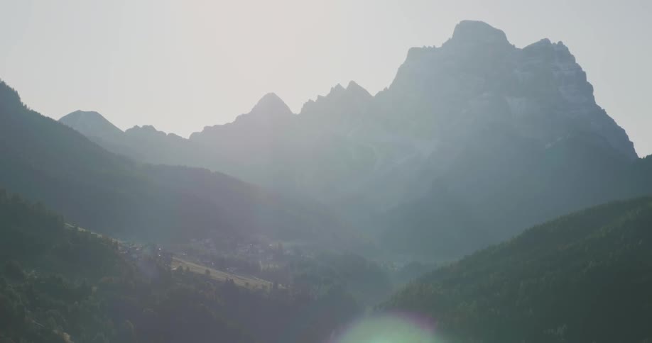 The sun shines through a hazy sky near mountains