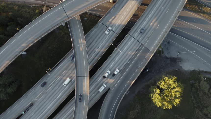 Ascending overhead view of vehicles driving on multi level highways and cloverleaf ramps