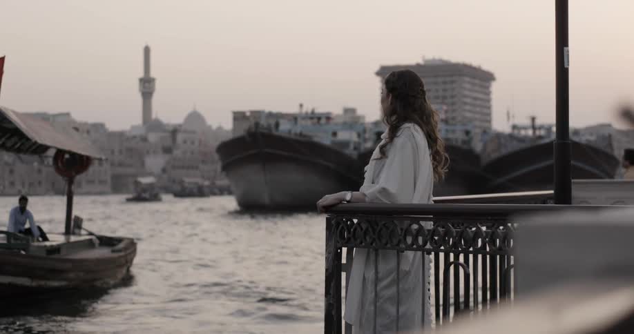 Woman standing on a balcony looks out at boats on water