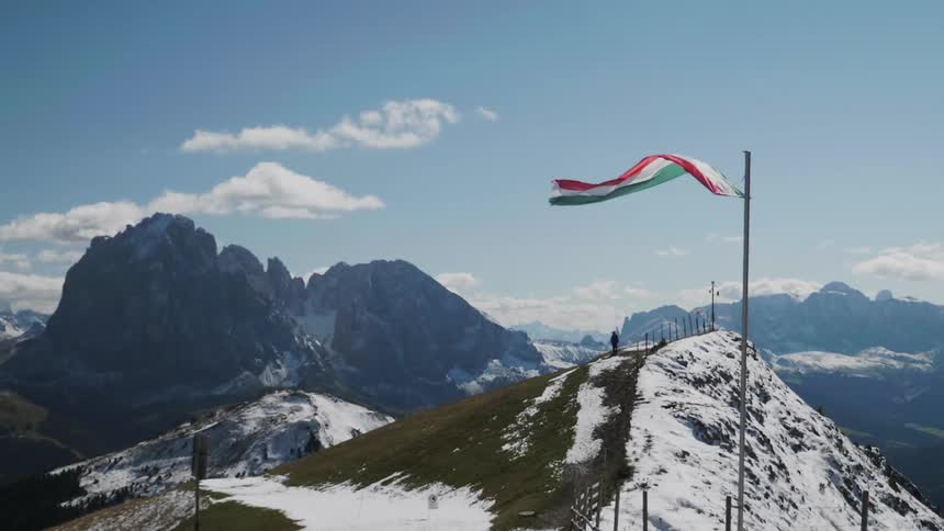 A flag is blown vigorously by the wind atop a snow-covered mountain