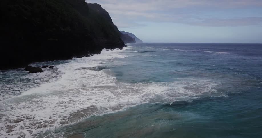 Waves crash and lap against steep cliffs during the day
