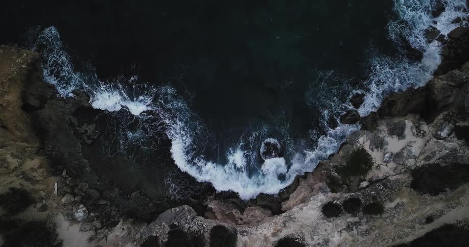 Waves crash against the base of cliffs during the day