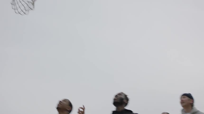 A man takes a jump shot as he plays basketball with others in an urban setting