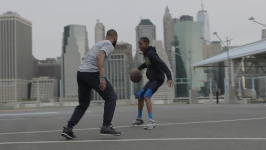 A young teenager goes one on one with an adult player on a basketball court